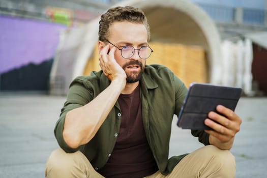 Shocked man reading information from tablet PC with frightened expression. Breaking news has caught him off guard. Facial expression conveys surprise, concern, and even panic. High quality photo