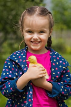 Cute happy little girl with of small duckling in the garden. Little girl holding a duckling in her hands.