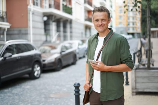 Lifestyle concept as handsome man is seen with mobile phone on charming streets of old city in Europe. urban backdrop evokes sense of history and culture, while man's presence adds modern touch to scene. . High quality photo