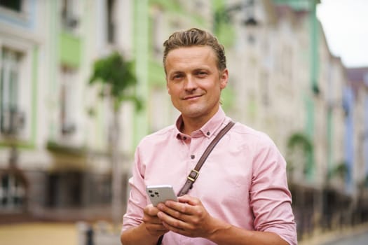 Mid aged man engaged in texting a message while being outdoors. With his mobile phone in hand, he utilizes digital communication to connect with others in the urban environment. High quality photo