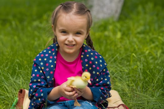 Cute happy little girl with of small duckling in the garden. Little girl holding a duckling in her hands.