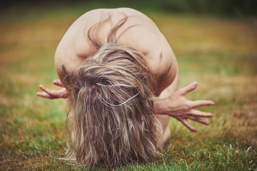 Naked woman curled in a fetus position in the evening forest.