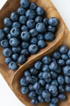 Ripe blueberries in a wooden interesting plate close-up on a white background. Delicious and healthy berry. View from above