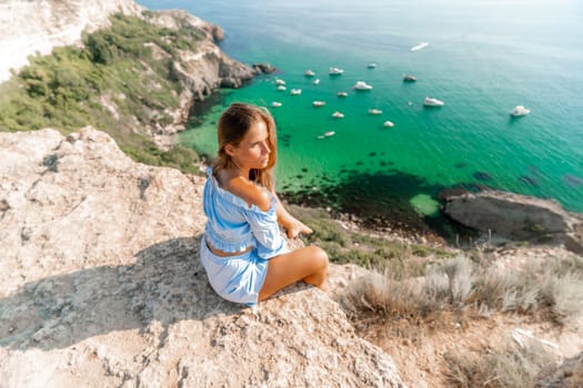 Woman travel sea. Happy woman in a beautiful location poses on a cliff high above the sea, with emerald waters and yachts in the background, while sharing her travel experiences.