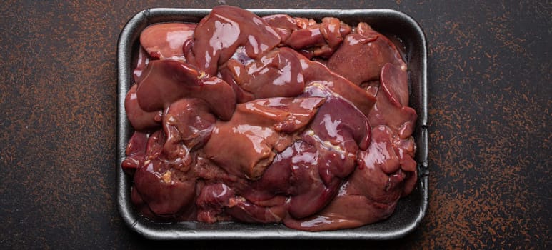 Raw chicken liver in black supermarket tray top view on dark rustic concrete background kitchen table. Healthy food ingredient, source of iron, folate and a variety of vitamins and minerals