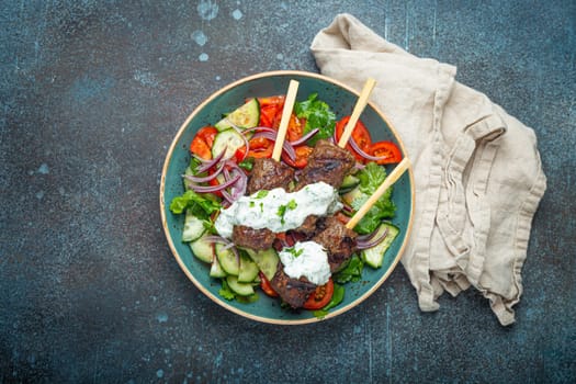 Grilled skewer meat beef kebabs on sticks served with fresh vegetables salad on plate on rustic concrete background from above. Traditional Middle Eastern and Turkish dish Kebab, space for text