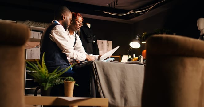 Tailors preparing fabric pattern for fashion collection manufacturing process, choosing perfect design on sketches. Couturier and assistant working on clothing line creation. Tripod shot.