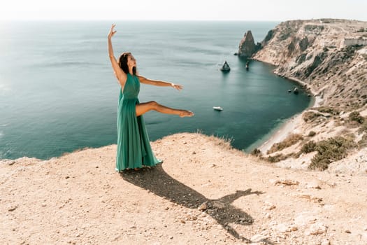 Woman green dress sea. Female dancer posing on a rocky outcrop high above the sea. Girl on the nature on blue sky background. Fashion photo