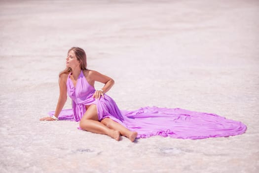 A woman in a pink dress sits on the salty shore of a pink lake and poses for a souvenir photo, creating lasting memories