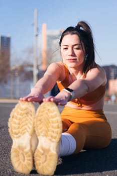 vertical photo of a caucasian woman stretching the legs sitting in an urban park, concept of health and sportive lifestyle