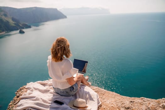 Freelance woman working on a laptop by the sea, typing away on the keyboard while enjoying the beautiful view, highlighting the idea of remote work