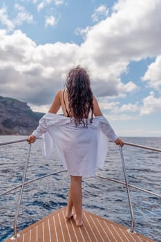 Woman on a yacht. Happy model in a swimsuit posing on a yacht against a blue sky with clouds and mountains.