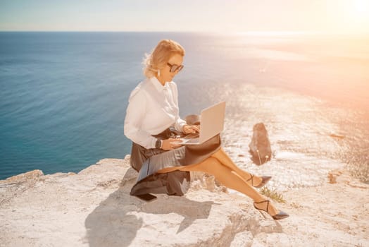 Business woman on nature in white shirt and black skirt. She works with an iPad in the open air with a beautiful view of the sea. The concept of remote work