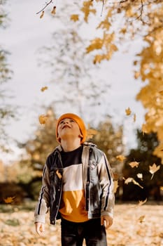 Kid having fun in autumn park with fallen leaves, throwing up leaf. Child boy outdoors playing with maple leaves