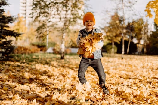 Kid having fun in autumn park with fallen leaves, throwing up leaf. Child boy outdoors playing with maple leaves