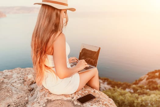 Freelance women sea working on the computer. Good looking middle aged woman typing on a laptop keyboard outdoors with a beautiful sea view. The concept of remote work