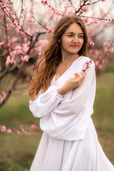 Woman peach blossom. Happy curly woman in white dress walking in the garden of blossoming peach trees in spring.