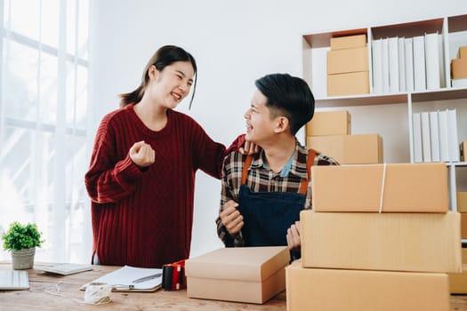 A young Asian couple shows delight and smiles on their faces when they see the sales volume and customer orders exceed expectations. sme or small business family concepts.