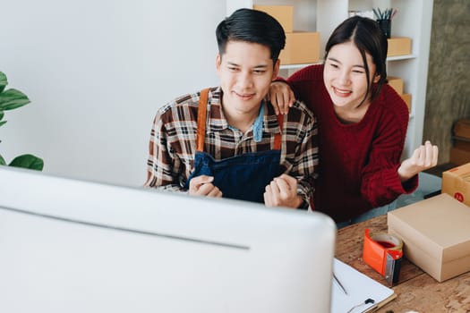 A young Asian couple shows delight and smiles on their faces when they see the sales volume and customer orders exceed expectations. sme or small business family concepts.