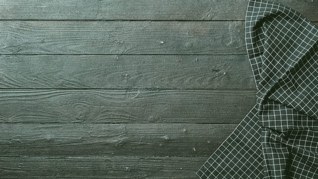 Dark wooden table with balck and white dark linen kitchen towel or textile napkin flat lay. Dark tablecloth on brown gray wood tabletop. Copy space for text. Can use as mock up for design.