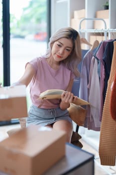 Portrait Of Asian Female Owner Of Fashion Store Checking Stock In Clothing Store With using notebook successful happy smile at small business, sme or ecommerce concepts.