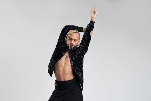 Man wearing women clothing dancing. Afro-american homosexual male wearing black skirt and jacket with sequins posing in photo studio on white background. Bearded gay with make up