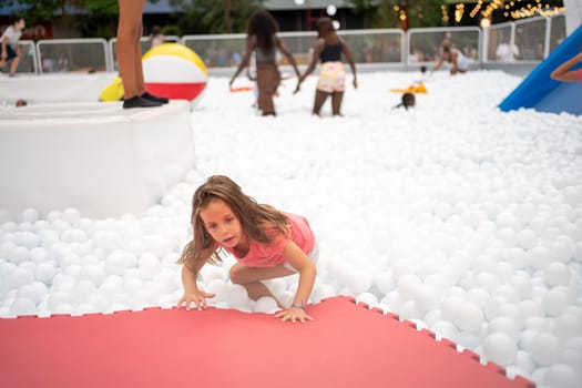 Happy little girl playing white plastic balls pool in amusement park. playground for kids. Active leisure for children.