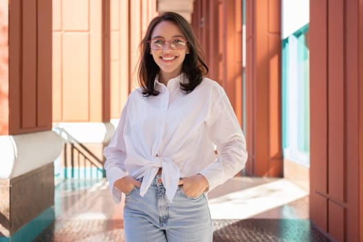 Successful smiling business woman brunette wearing eyeglasses hands in pocket. Modern businesswoman smile standing outdoor dressed white shirt and jeans. Business woman happy positive emotions