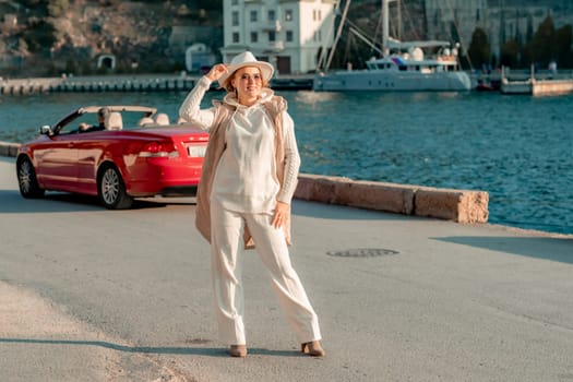 Portrait of a blonde convertible. Fashionable attractive woman with blond hair in a white hat on the background of a red car and the sea
