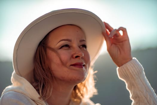 Happy blonde woman in a white suit and hat posing at the camera against the backdrop of the sea.