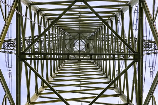 Steel beams, wires and a bird's nest in a huge power pole photographed directly from below against the sky