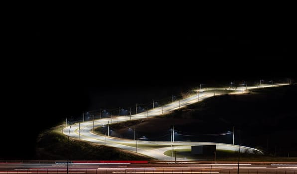 A stunning night view of a highway with long exposure light trails from passing cars. The road diversion is brightly illuminated, creating a captivating scene. The surrounding areas are dark, providing ample space for text or graphics. .
