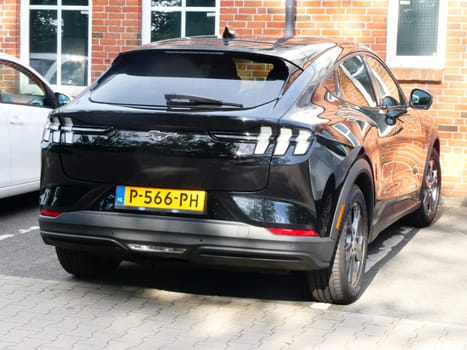 Uelsen, Germany - June 27 2023 A black Ford Mustang Mach-E parked in front of a brick wall. The wall is reflected in the car. This Mustang is all electric