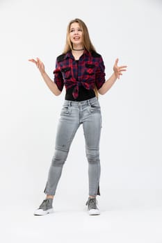 The woman is standing and posing against a white background. She is wearing light tight jeans and a krfata shirt tied in a knot. The girl has her arms spread at her sides and poses with a disgruntled expression. Long-haired girl with loose hair.