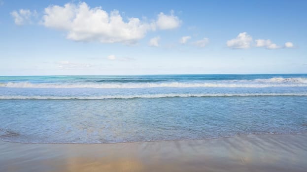 Golden sand and blue ocean water with white clouds. Karon Beach. In places, high waves and splashes. Blue sky. The sun's rays are reflected on the sand. White foam from the waves. Thailand