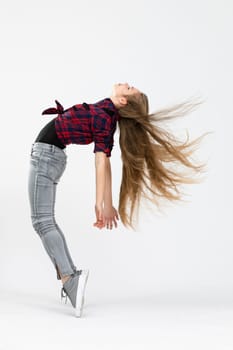 The girl is wearing fitted jeans, a checked shirt and sports shoes. Young woman poses for the photo and performs a difficult acrobatics by standing on tiptoe and arching her back. The girl's hair can be seen moving and flying in the air.