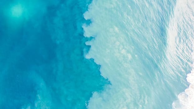 Top view of light blue water with white sand. Waves raise sand and a mix with turquoise water is obtained. Shadows from clouds on a clear ocean. Clear sea. Gradient of blue. The background photo