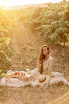 Woman picnic vineyard. Romantic dinner, fruit and wine. Happy woman with a glass of wine at a picnic in the vineyard on sunny day, wine tasting at sunset