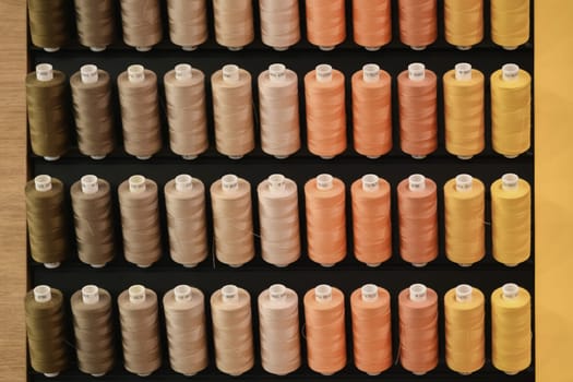 A row of multi-colored thread spools in brown orange yellow tones