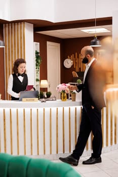 Businessman with passport id papers preparing to do check in for room reservation, reviewing documents at front desk reception. Client travelling for work to attend official meetings.