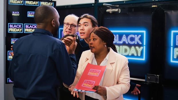 Black Friday shopping madness. Group of mad diverse clients push security guard to enter first into shopping center. Bargain hunters going crazy to get best deals, seasonal discounts.