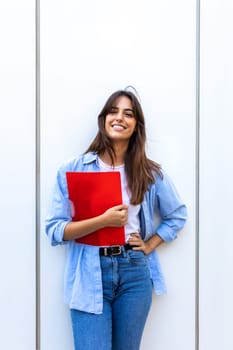 Happy, smiling female college student looking at camera holding red folder. Vertical image. Education concept.