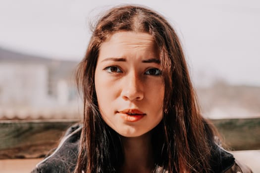 Happy young smiling woman with freckles outdoors portrait. Soft sunny colors. Outdoor close-up portrait of a young brunette woman and looking to the camera, posing against nature background.