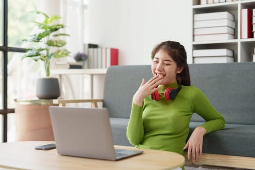 Young asian relaxed smiling pretty woman relaxing with laptop at home. Female feeling joy enjoying with mobile phone on cozy couch.