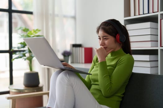 Young asian relaxed smiling pretty woman relaxing with laptop at home. Female feeling joy enjoying with mobile phone on cozy couch.