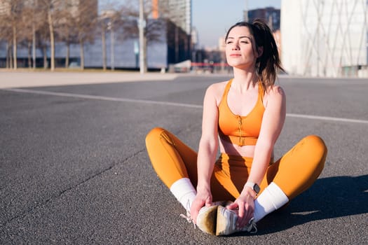 caucasian woman stretching legs sitting in an urban park, concept of health and sportive lifestyle, copy space for text