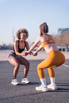 vertical photo of two multiethnic female friends exercising together in an urban park, concept of friendship and sportive lifestyle