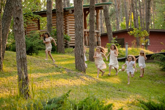 Group of cheerful tween girls playing in green summer park, running together among tall trees on sunny day. Happy healthy childhood concept