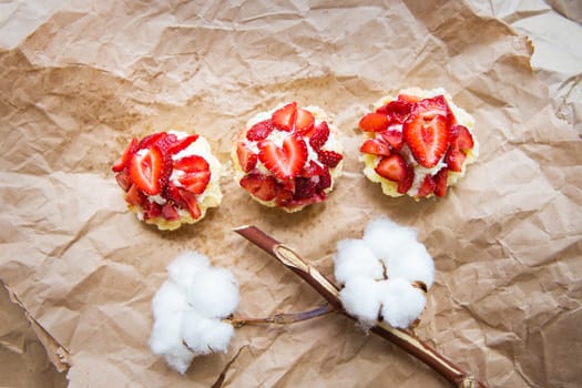 Beautiful cupcakes with strawberries along with a branch of cotton lies on kraft paper.