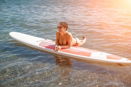 Woman sup sea travel. Sports girl on a surfboard in the sea on a sunny summer day. In a black bathing suit, he sits on a sapa in the sea. Rest on the sea